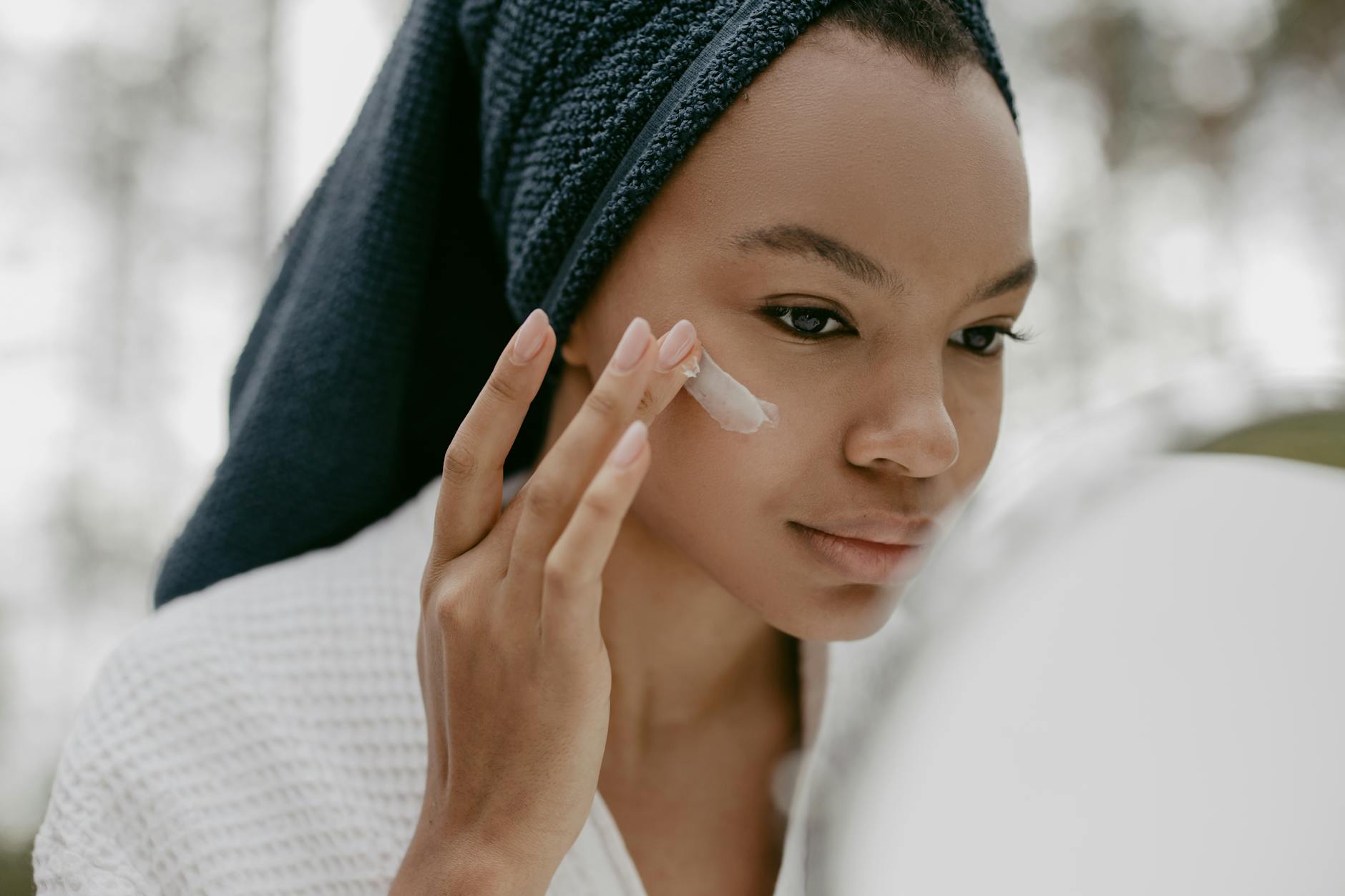 Femme appliquant une creme hydratante sur son visage devant un miroir